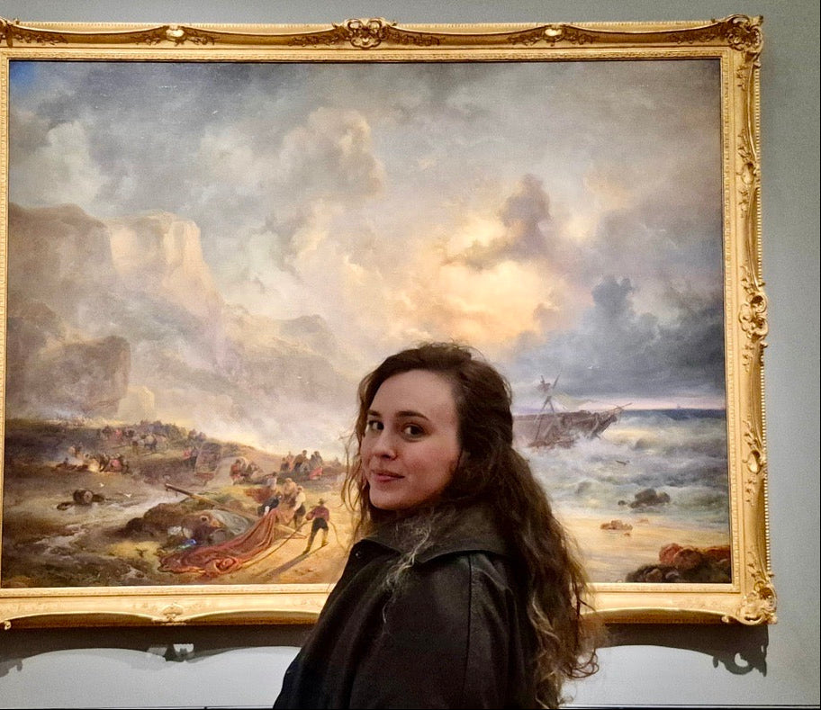 Woman standing in front of a large painting with a gold frame.