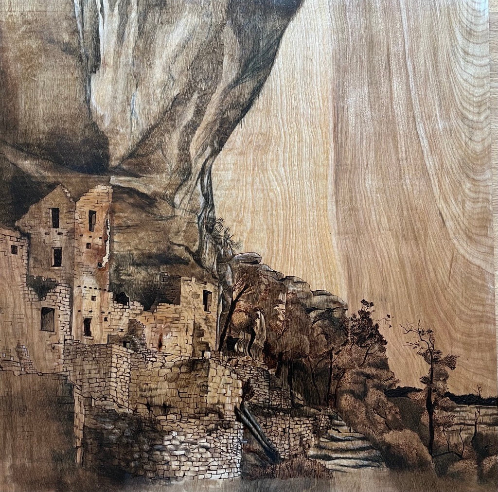 Artistic depiction of a stone village with cliffs and trees on a wooden surface.